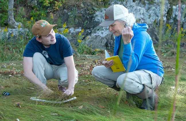 Pam Morgan and Robyn Rollo crouch down to survey a section of the marsh for invertibretes 